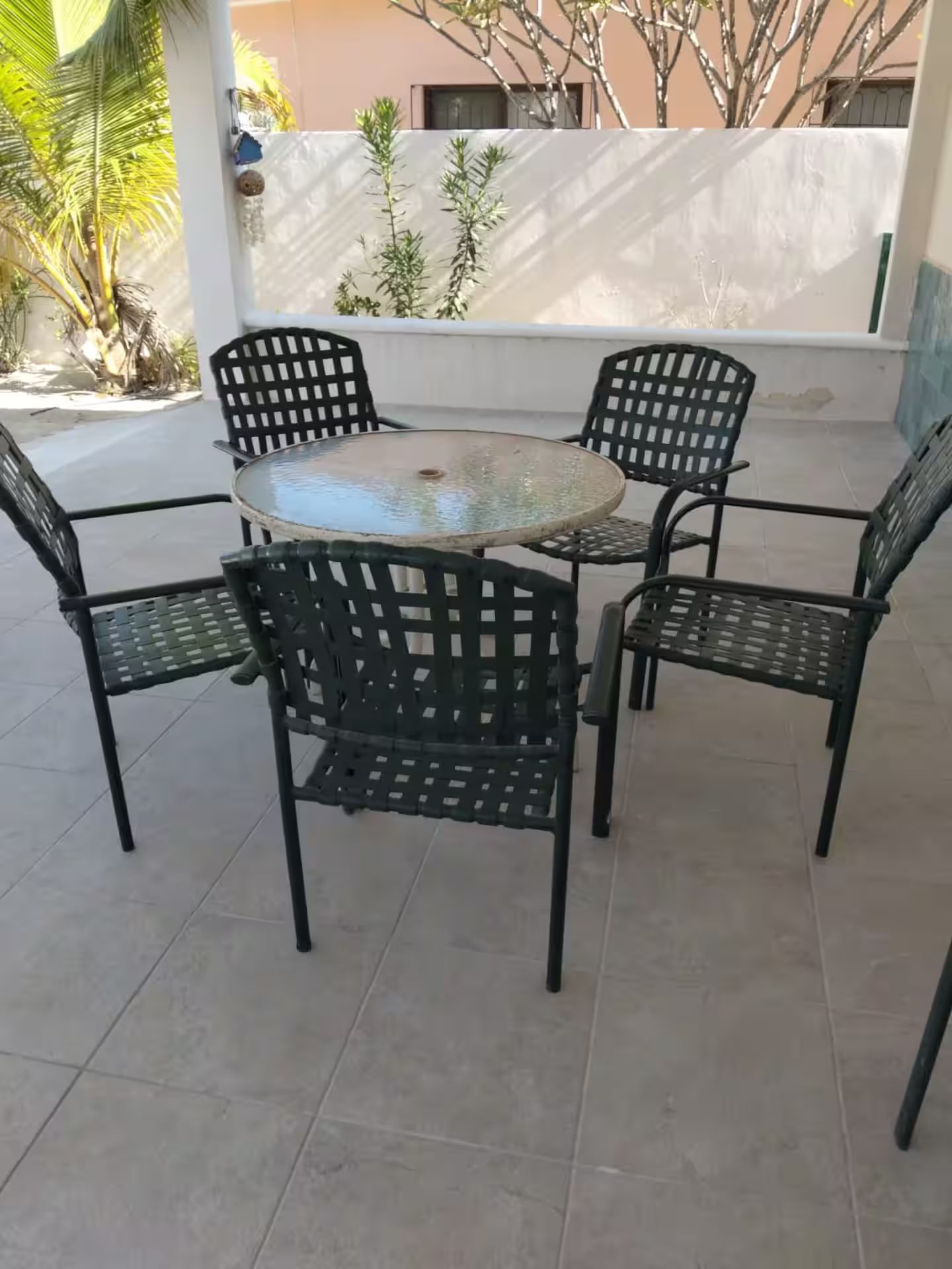 Una mesa redonda de vidrio con estructura metálica, rodeada por cuatro sillas con diseño de celosía.