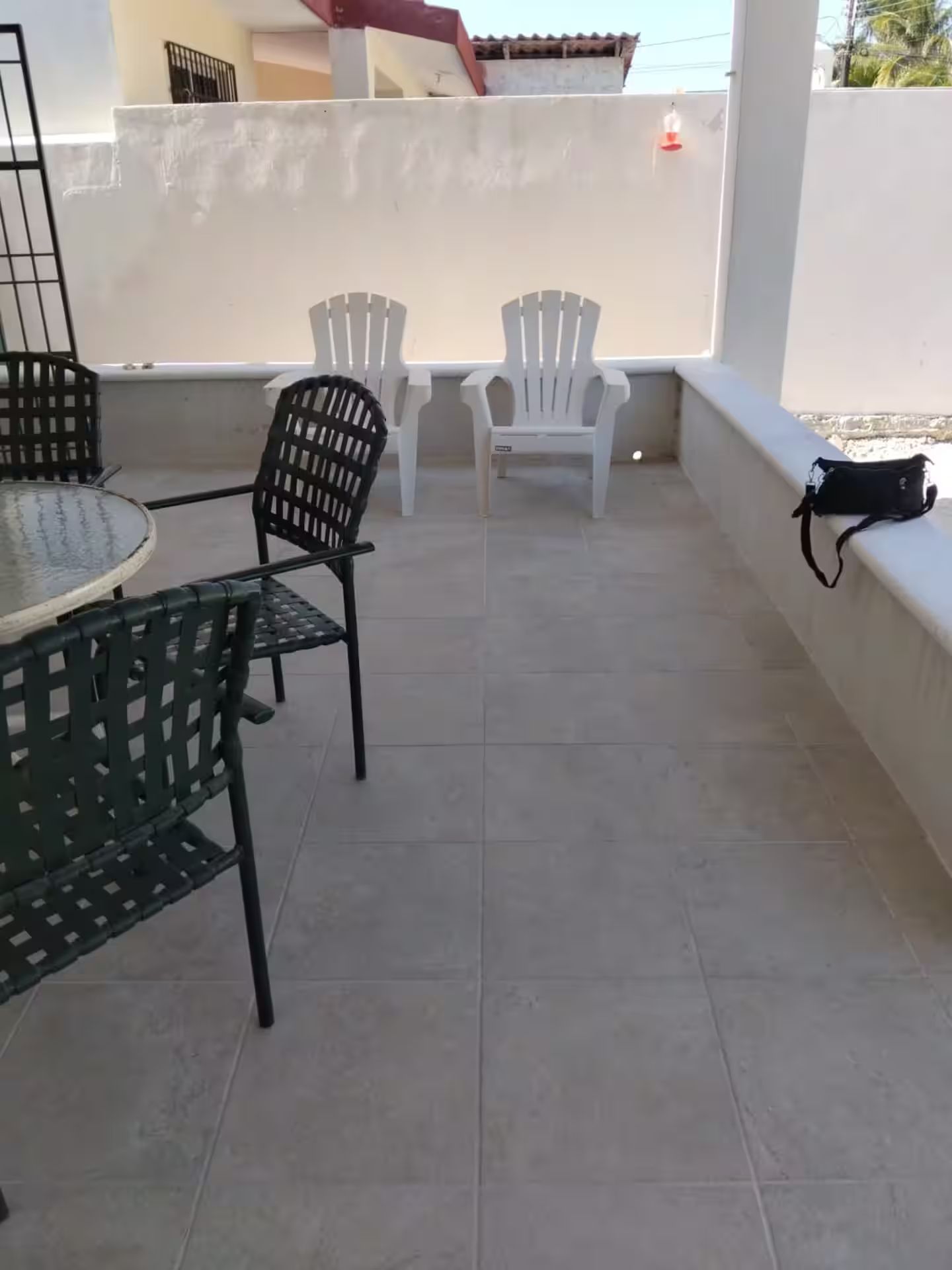 A balcony with a round table and chairs, a white wall, and a bag on the railing.
