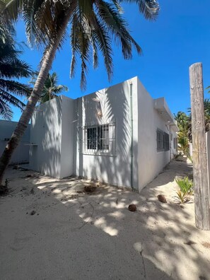 A white building with barred windows and a concrete ground, surrounded by palm trees and a clear blue sky. - Casa brisas de Chelem colibrí (Chelem)