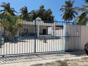 A gated area with a building, palm trees, and a clear sky. - Casa brisas de Chelem colibrí (Chelem)