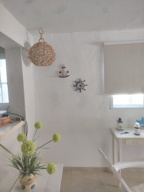 A room with a white wall, a hanging woven light fixture, a small ship's wheel decoration, a desk with a lamp, and a potted plant with green flowers. - Casa brisas de Chelem colibrí (Chelem)