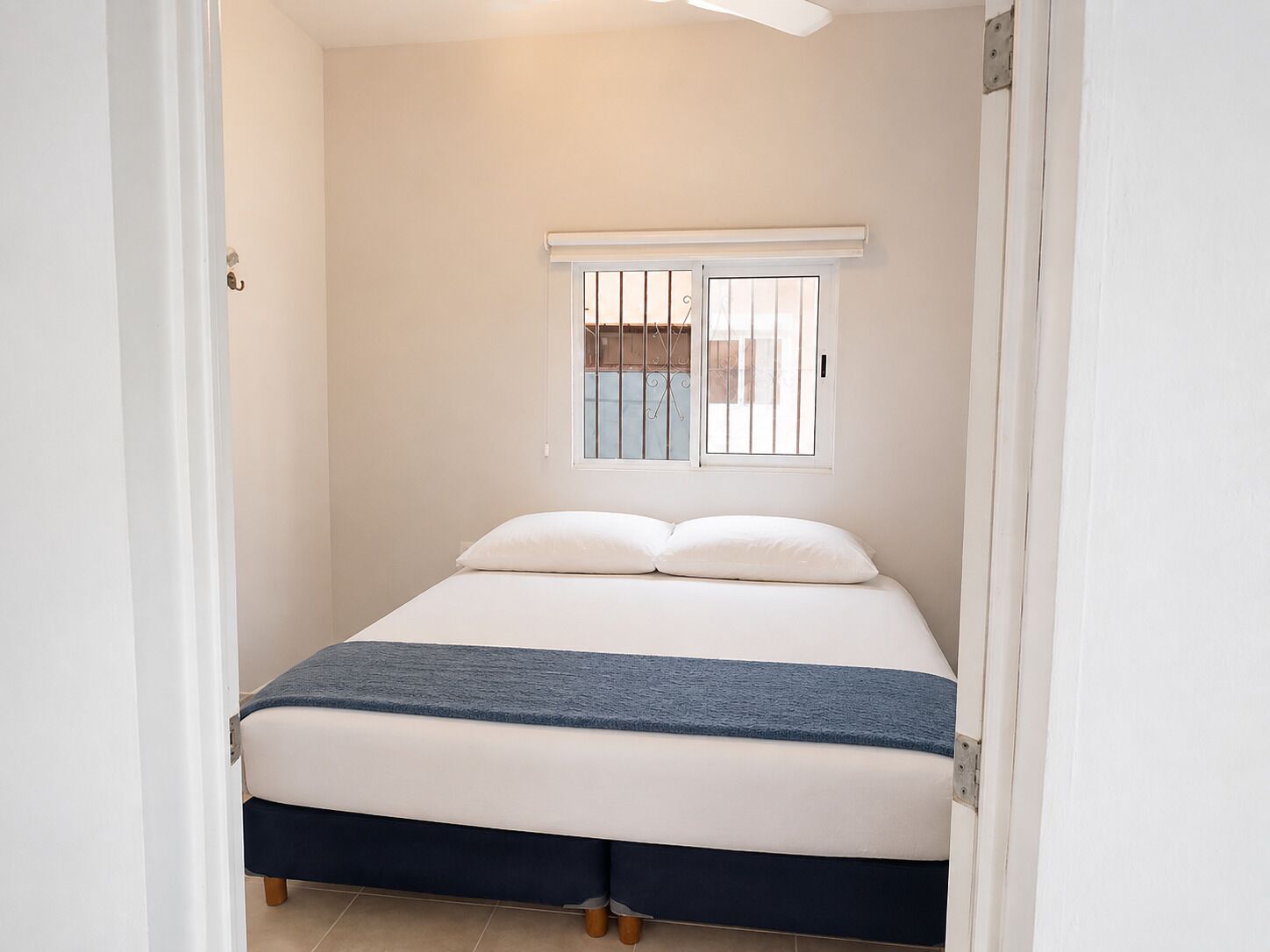 A bedroom with a bed, a window with bars, and a ceiling fan.