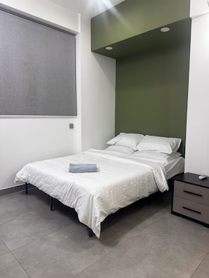 A bedroom with a bed, a nightstand, a window with blinds, and a green accent wall.
