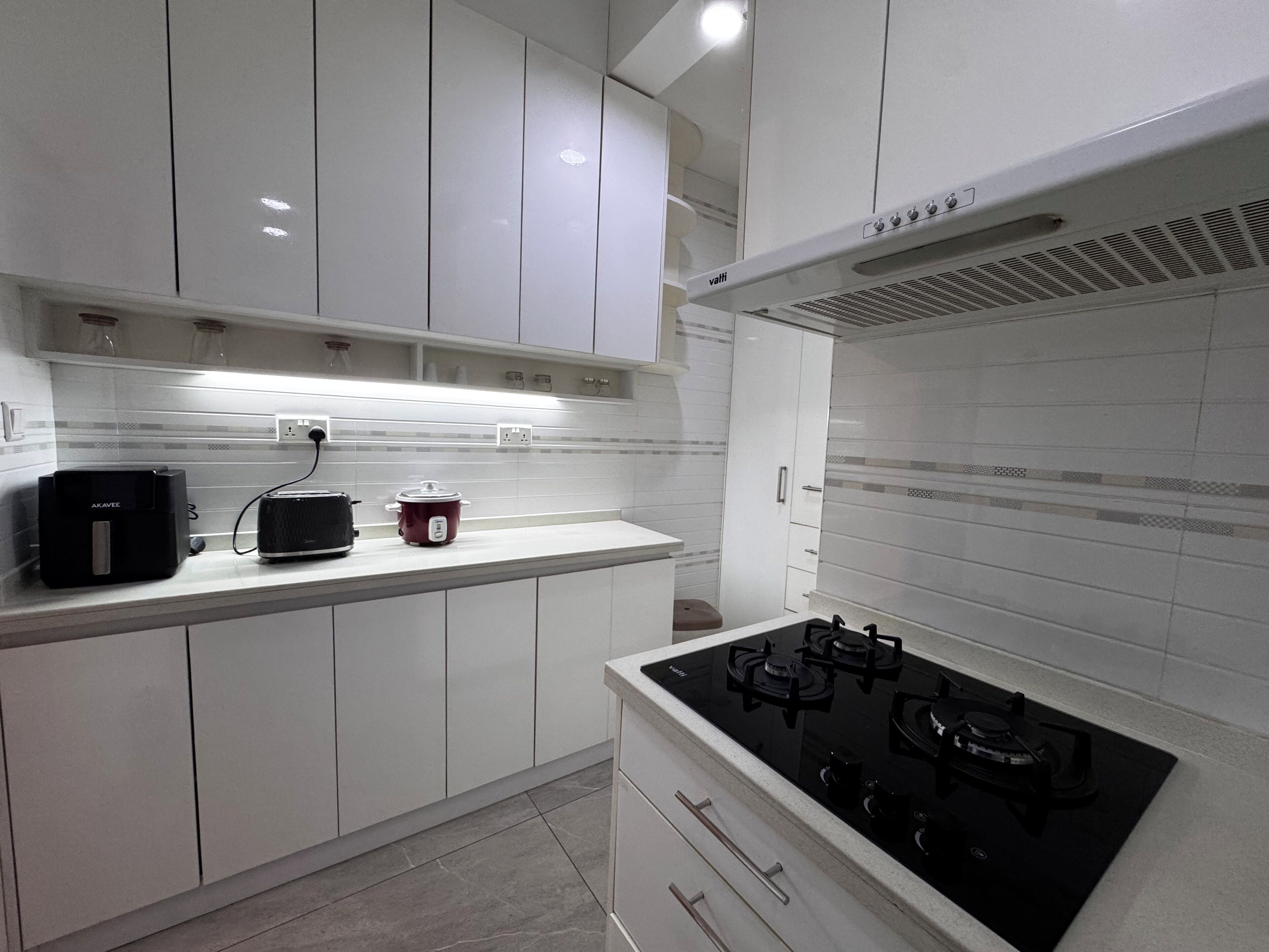 A modern kitchen with white cabinets, a black stove, and a red slow cooker.