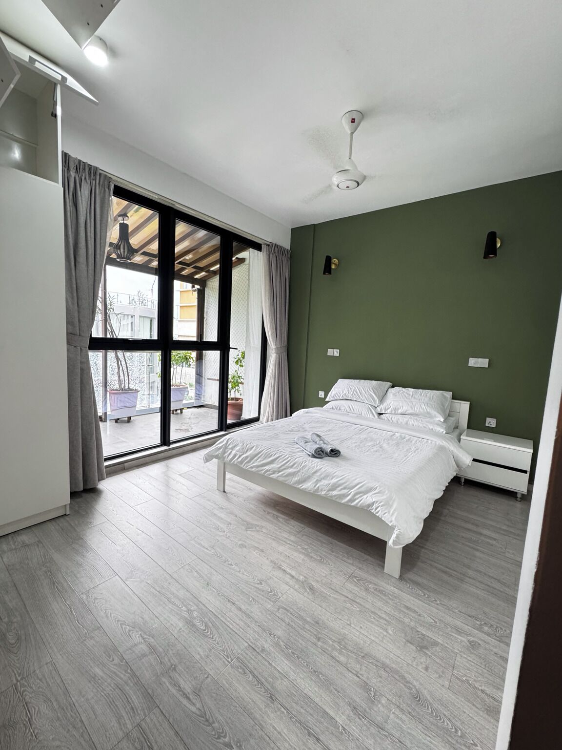 Un dormitorio con cama, ventilador de techo, ventana con cortinas y vistas al exterior.