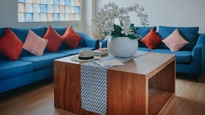 A living room with a blue sofa, a wooden coffee table, and a large window with a view.