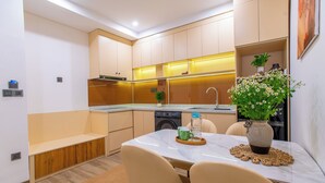 A modern kitchen with built-in appliances, a dining area with a table and chairs, and a small seating area. - Lavi Residence (Da Nang)