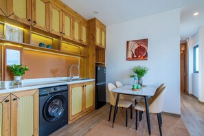 A modern kitchen with wooden cabinets, a washing machine, and a dining area with a table and chairs. - Lavi Residence (Da Nang)