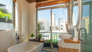 A modern bathroom with a freestanding bathtub, a sink, and a large window offering a city view. - Lavi Residence (Da Nang)