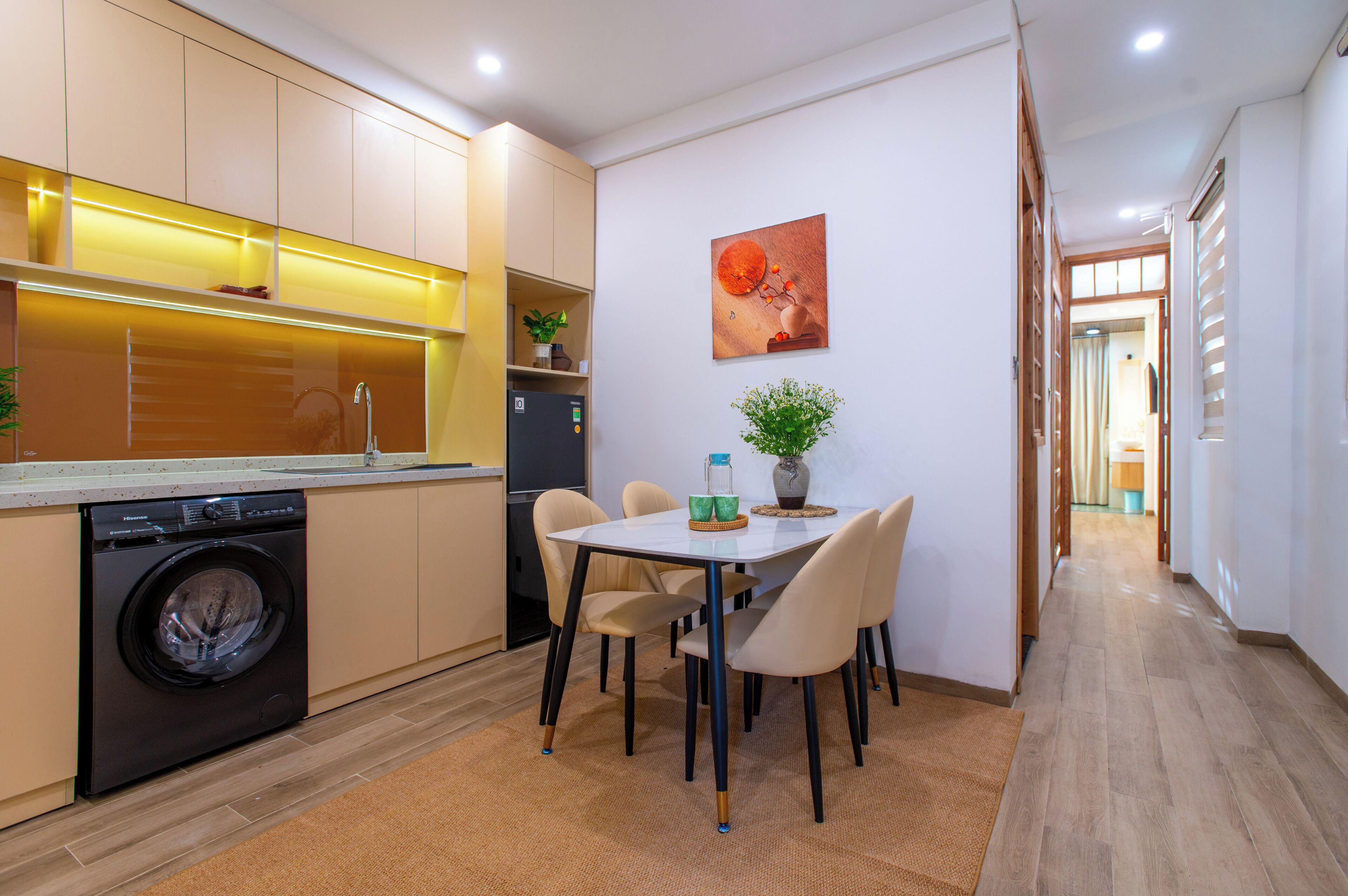 A modern kitchen with a washing machine, a dining table with chairs, and a hallway leading to another room.