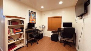 A room with a desk, two chairs, a bookshelf, a television, and a window with blinds.