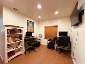 A room with a desk, two chairs, a bookshelf, a television, and a window with blinds.