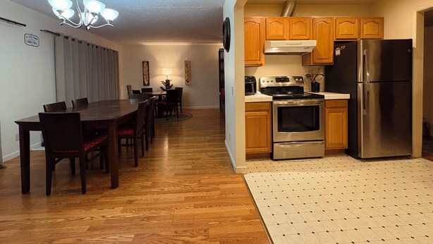 A modern kitchen with wooden cabinets, stainless steel appliances, and a dining area with a dark wooden table and chairs.