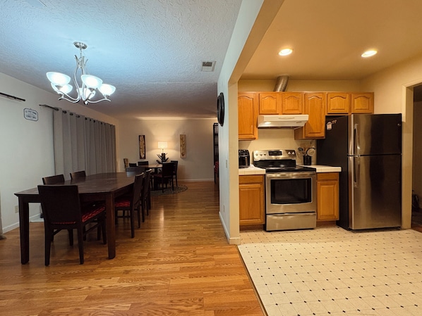 A modern kitchen with wooden cabinets, stainless steel appliances, and a dining area with a dark wooden table and chairs.