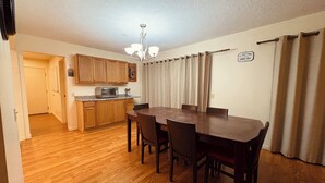 A dining area with a wooden table and chairs, a kitchen with wooden cabinets, a microwave, and a chandelier.