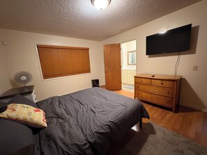 A bedroom with a bed, a dresser, a television, and a window with blinds.