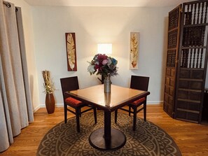 A dining area with a wooden table, four chairs, a vase with flowers, and decorative wall art.