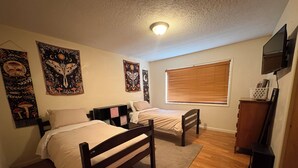 A bedroom with two single beds, a wooden floor, a window with blinds, and wall art.