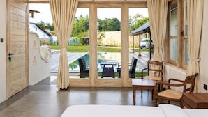 A room with a bed, a dining table, and chairs, a view of a swimming pool, and a door leading outside.