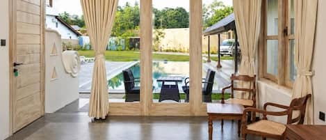 A room with a bed, a dining table, and chairs, a view of a swimming pool, and a door leading outside.