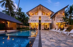 A resort with a pool, lounge chairs, and a two-story building with balconies. - The Oceans Edge (Dodanduwa)