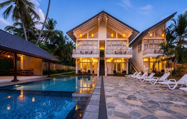 A resort with a pool, lounge chairs, and a two-story building with balconies. - The Oceans Edge (Dodanduwa)