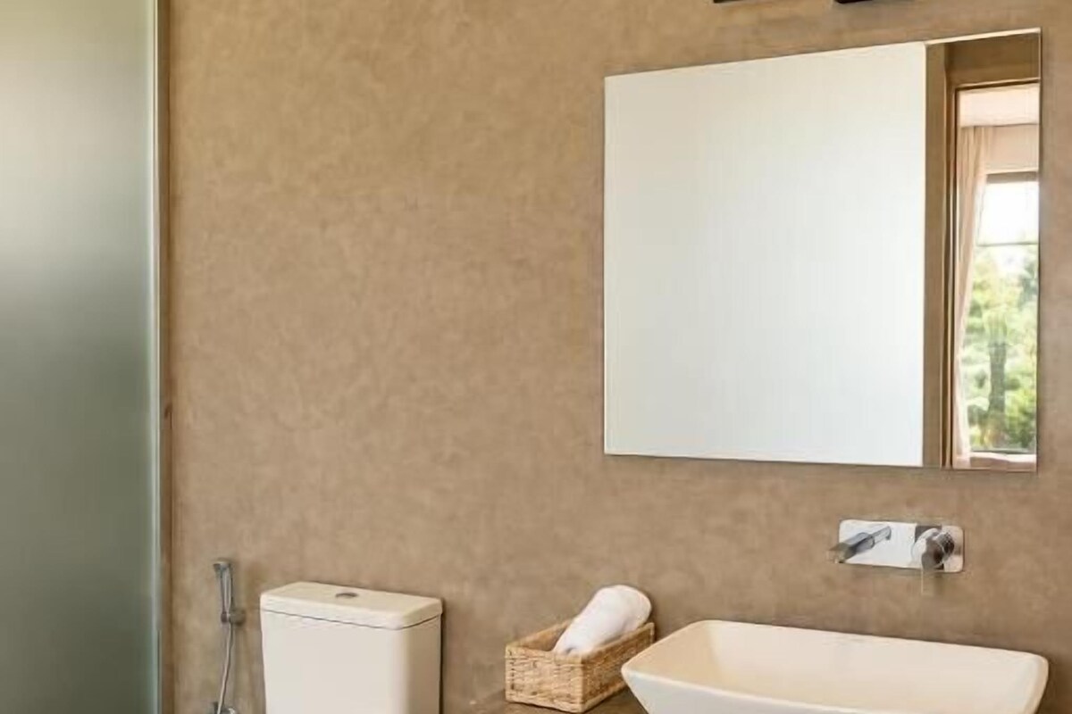 Un baño con inodoro, lavamanos, espejo y toallero.