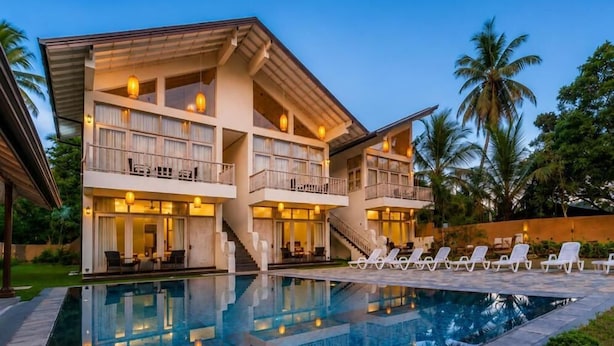 A multi-story hotel with a swimming pool, outdoor seating, and palm trees.