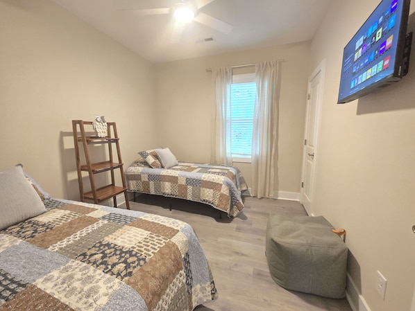 Quarto com duas camas, televisão, janela com cortinas e escada de madeira.