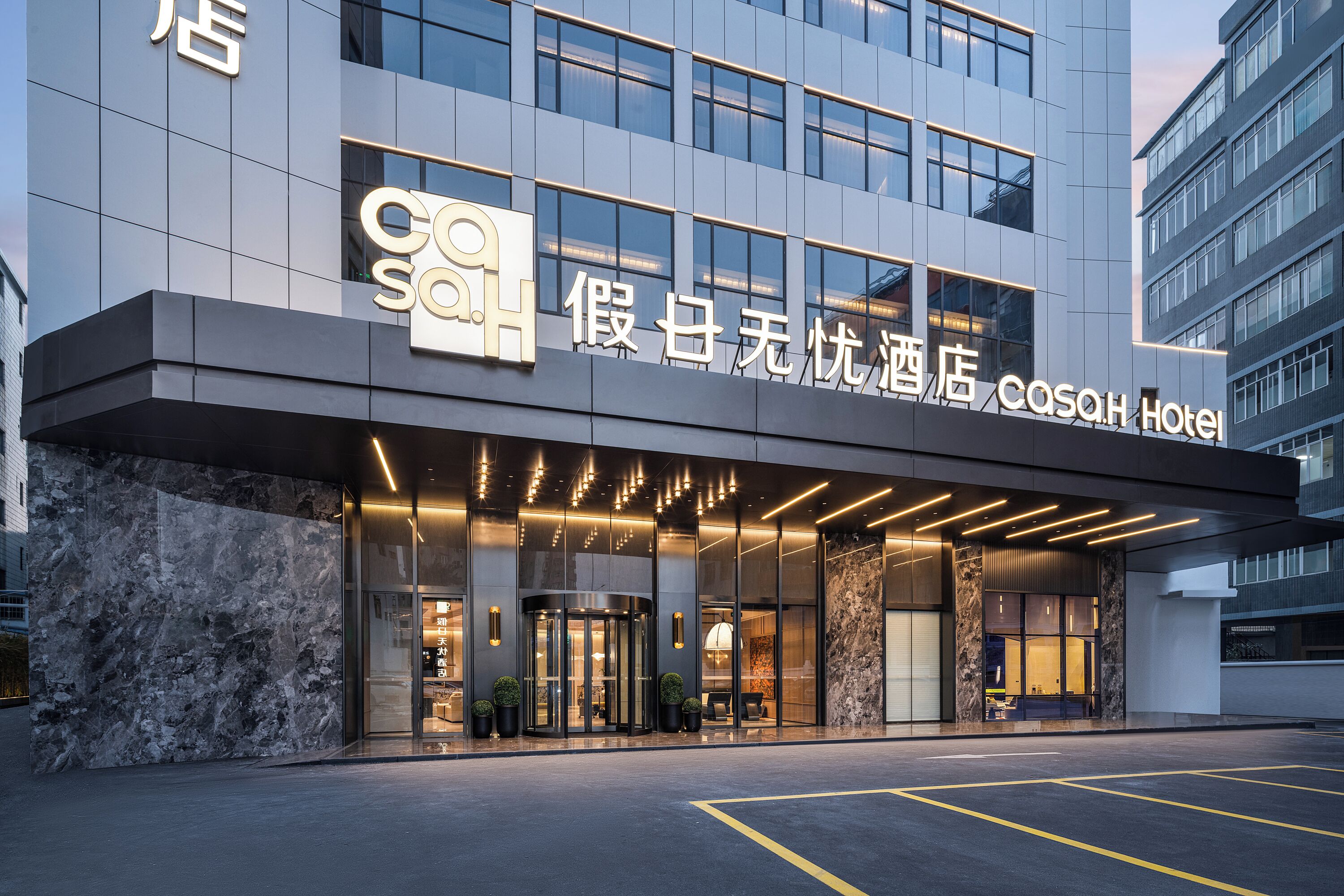 A modern hotel entrance with a glass facade, illuminated signage, and a marble-textured wall.