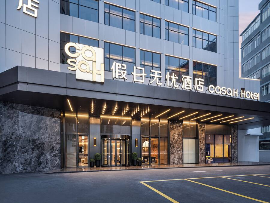 A modern hotel entrance with a glass facade, illuminated signage, and a marble-textured wall.