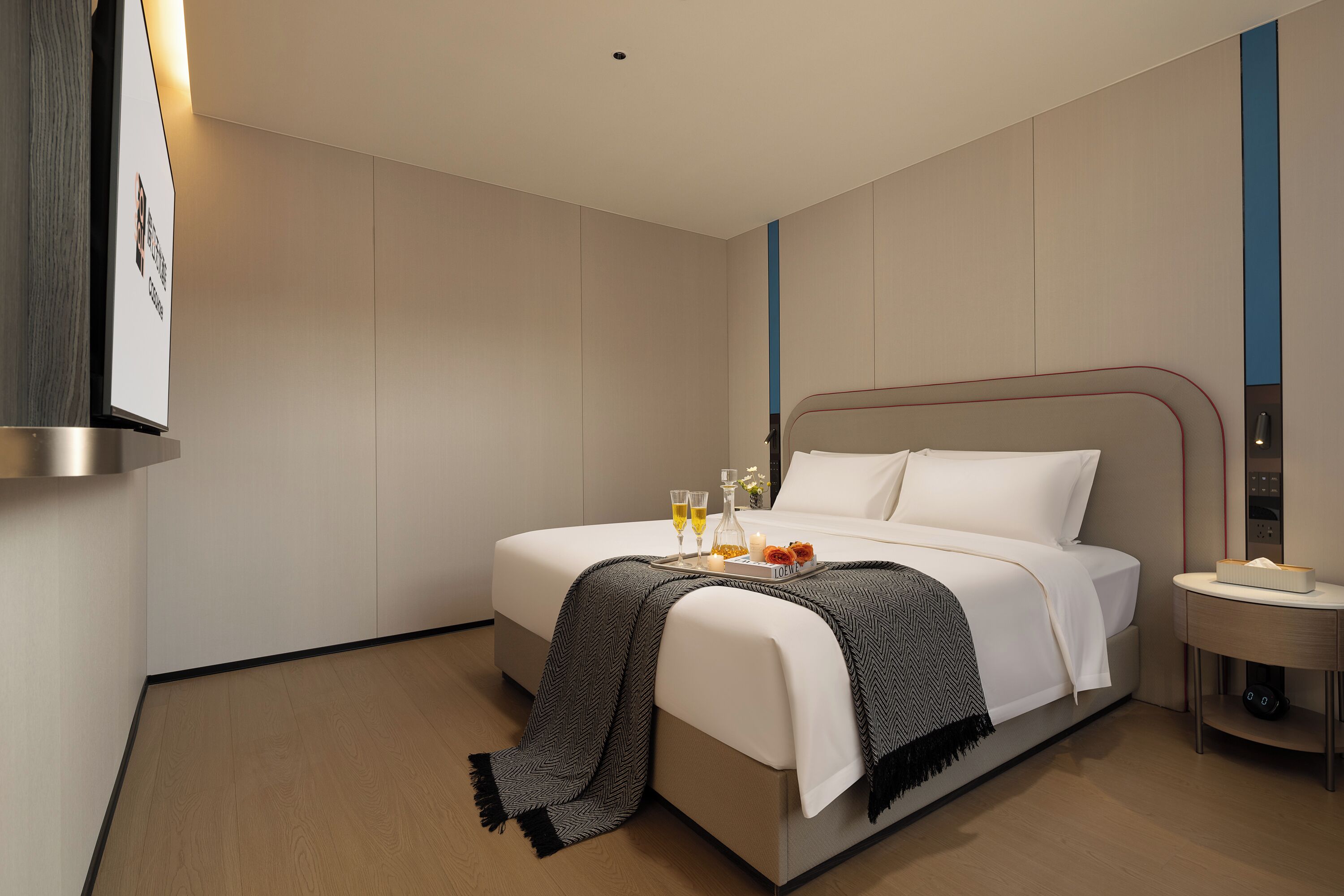 Habitación de hotel moderna con una cama bien hecha, una mesita de noche con lámpara y un televisor de pared.