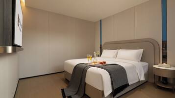Habitación de hotel moderna con una cama bien hecha, una mesita de noche con lámpara y un televisor de pared.