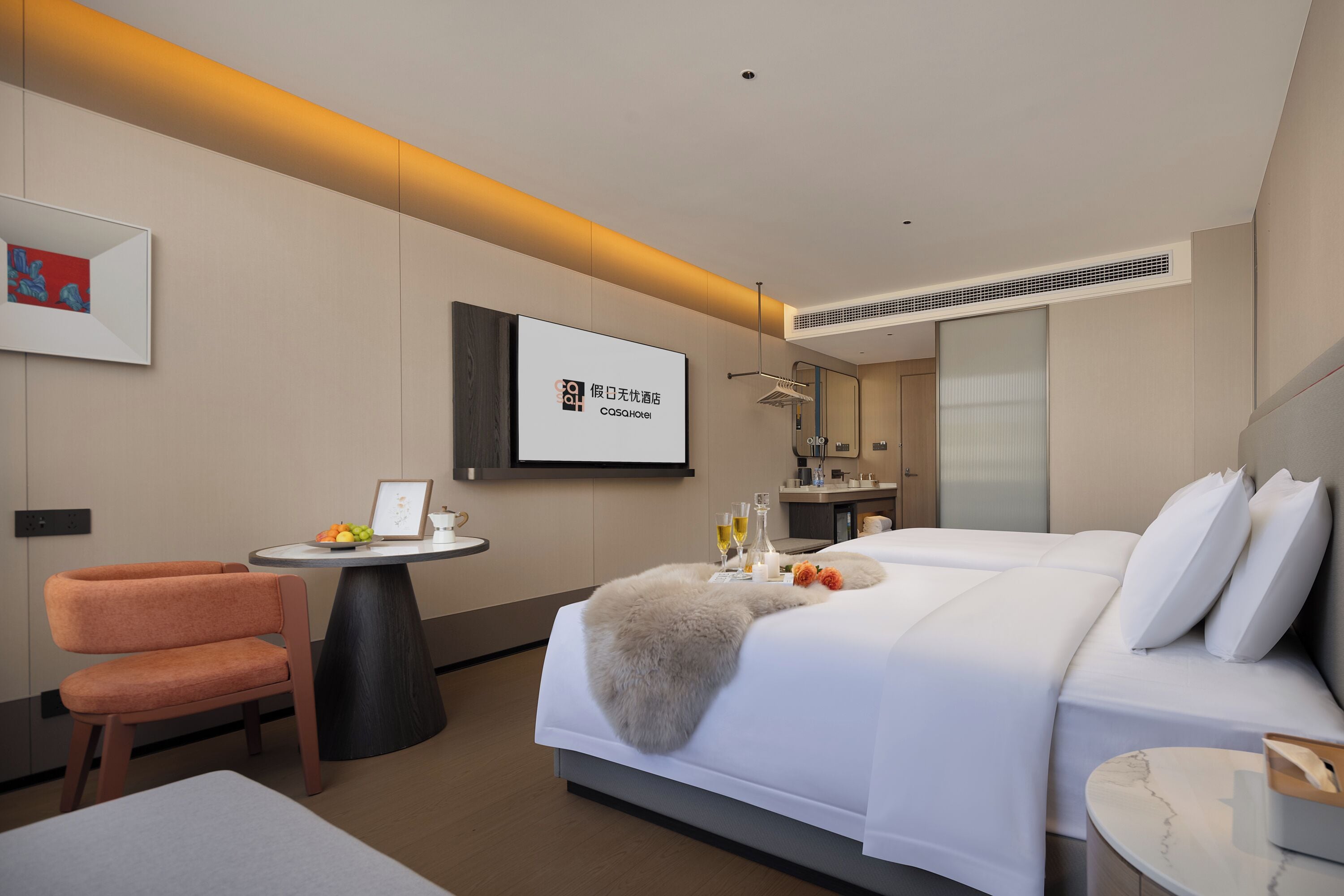 A hotel room with a bed, a desk, a chair, and a television displaying the hotel's name.