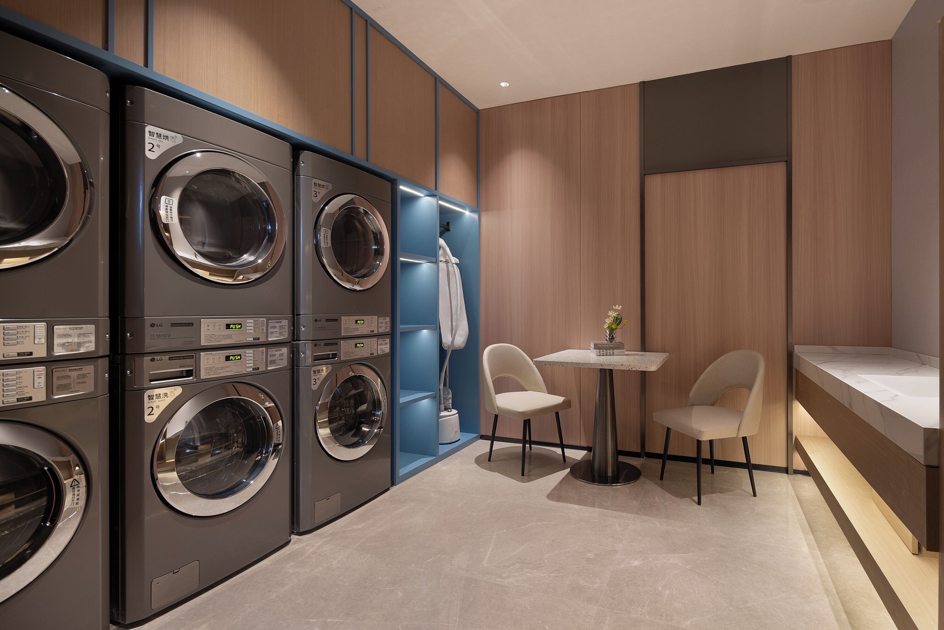 A laundry room with multiple washing machines, a small table with chairs, and a towel rack.