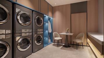 A laundry room with multiple washing machines, a small table with chairs, and a towel rack.
