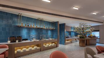 Un moderno vestíbulo de hotel con una pared de azulejos azules, una zona de buffet con mostradores de comida y diferentes disposiciones de asientos.