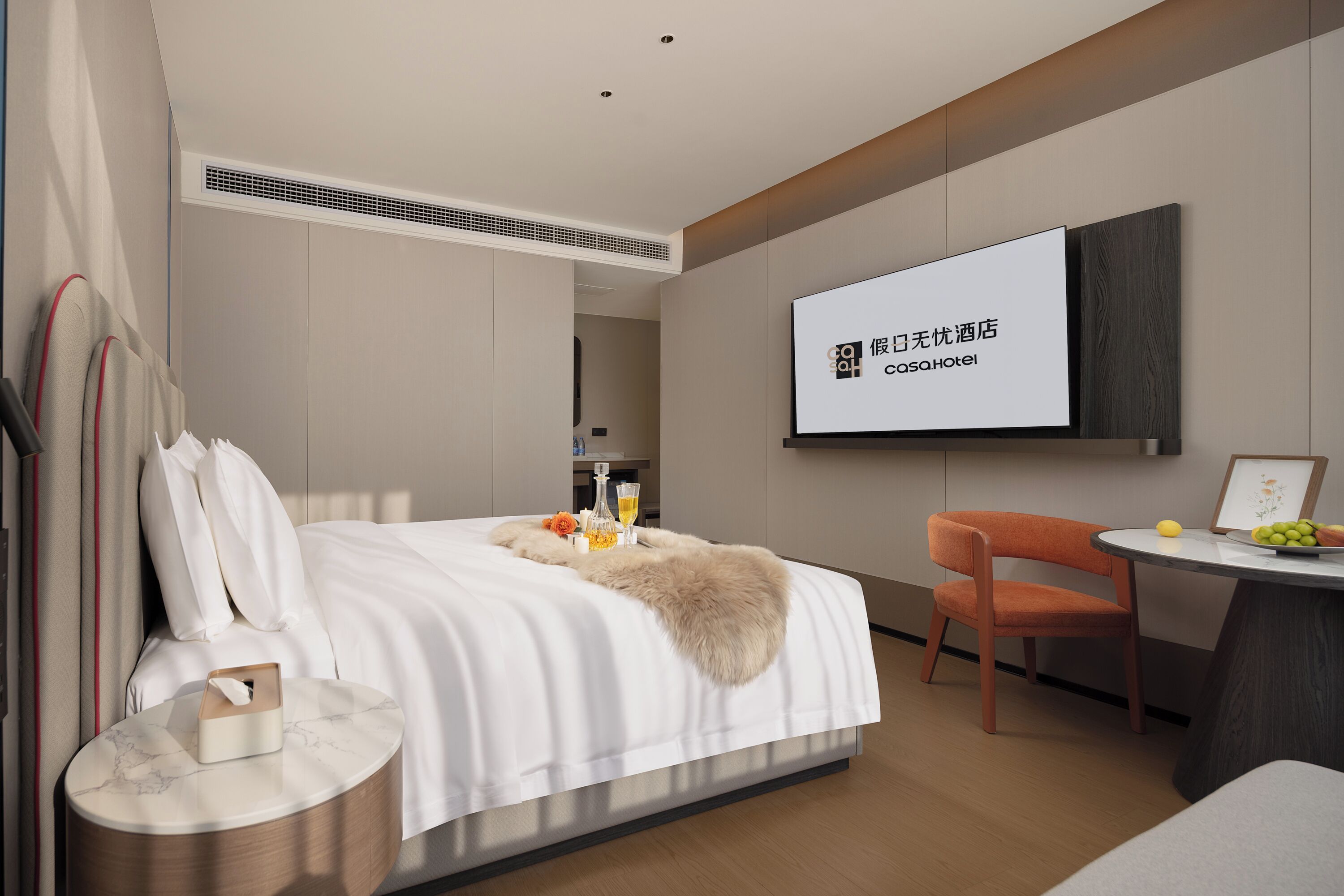 A modern hotel room with a bed, a desk, and a television screen displaying hotel branding.