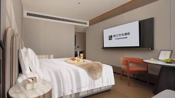 A modern hotel room with a bed, a desk, and a television screen displaying hotel branding.