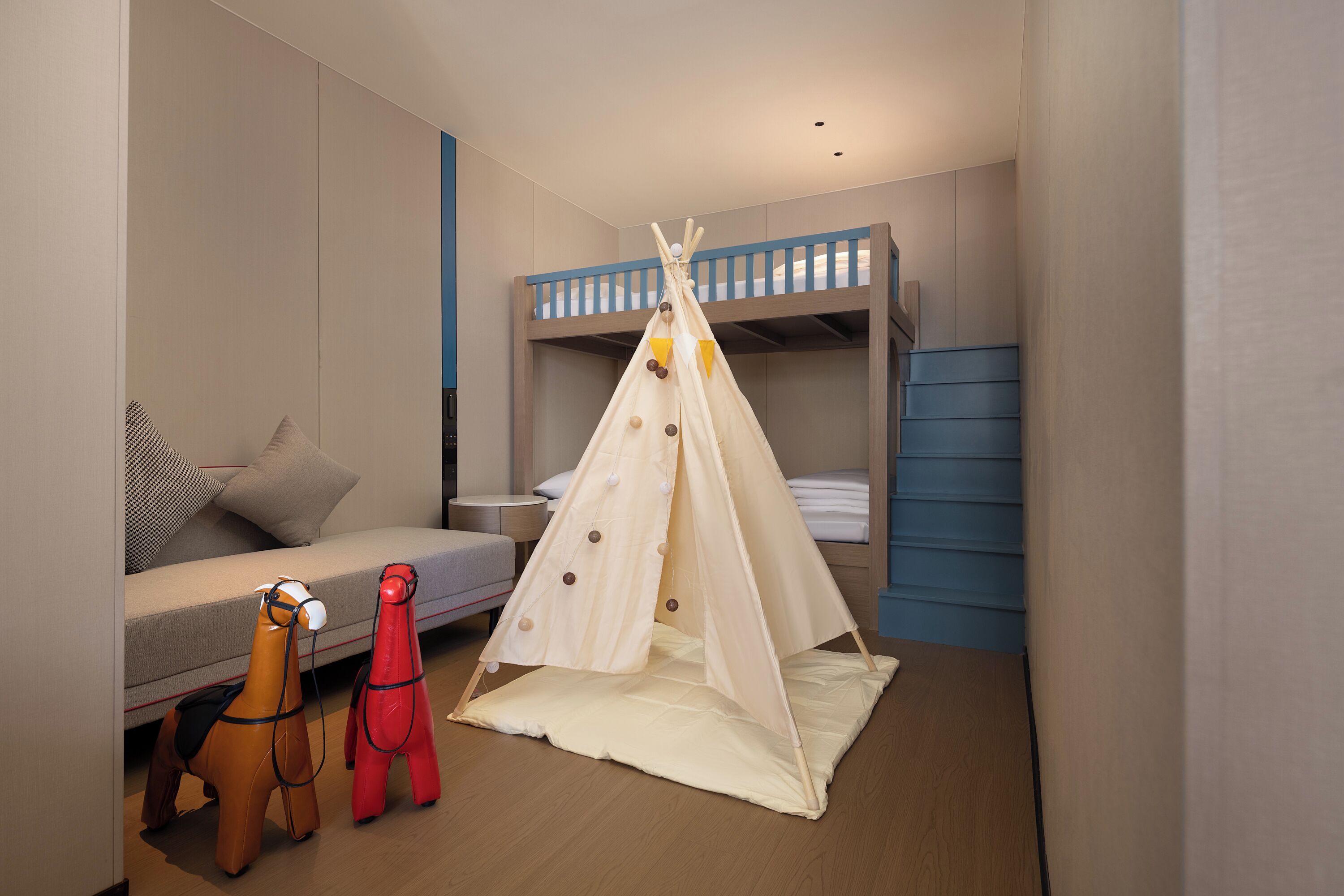 A child's bedroom with bunk beds, a sofa, a play tent, and two toy horses.