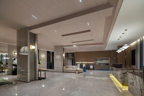 A modern hotel lobby with a reception desk, seating area, and a visible elevator.