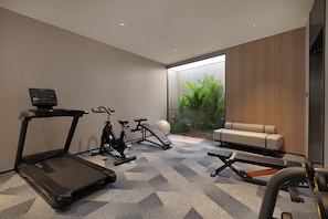 A modern home gym with exercise equipment, a sofa, and a view of greenery through a glass door.