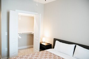 Ein Hotelzimmer mit Bett, Nachttisch, Lampe und einem Schrank mit Kleidung.