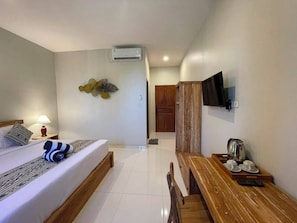 A hotel room with a bed, a wooden bench, a TV mounted on the wall, and an air conditioning unit. - Skyline Sanur (Denpasar)