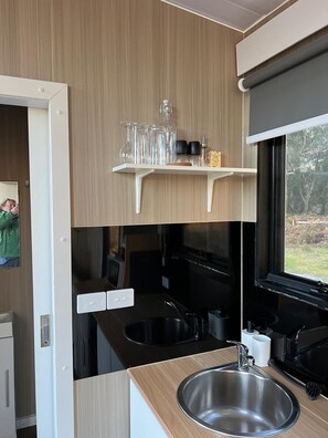 A modern kitchen with a stainless steel sink, wooden countertop, and a window with a view of greenery.