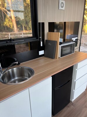 Una kitchenette compacta con un lavamanos de acero inoxidable, un microondas y una pequeña encimera.