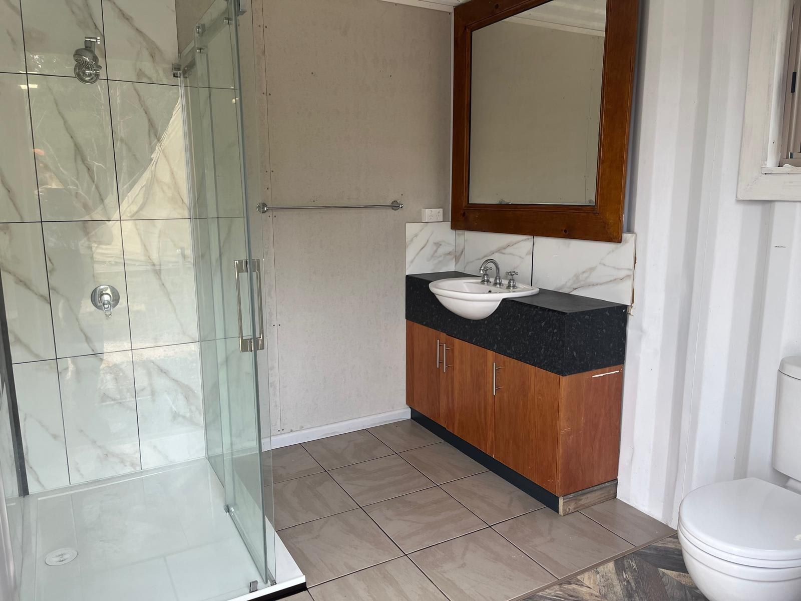 Une salle de bain avec une douche à parois de verre, un lavabo avec un plan de toilette en marbre, des meubles en bois et des toilettes.