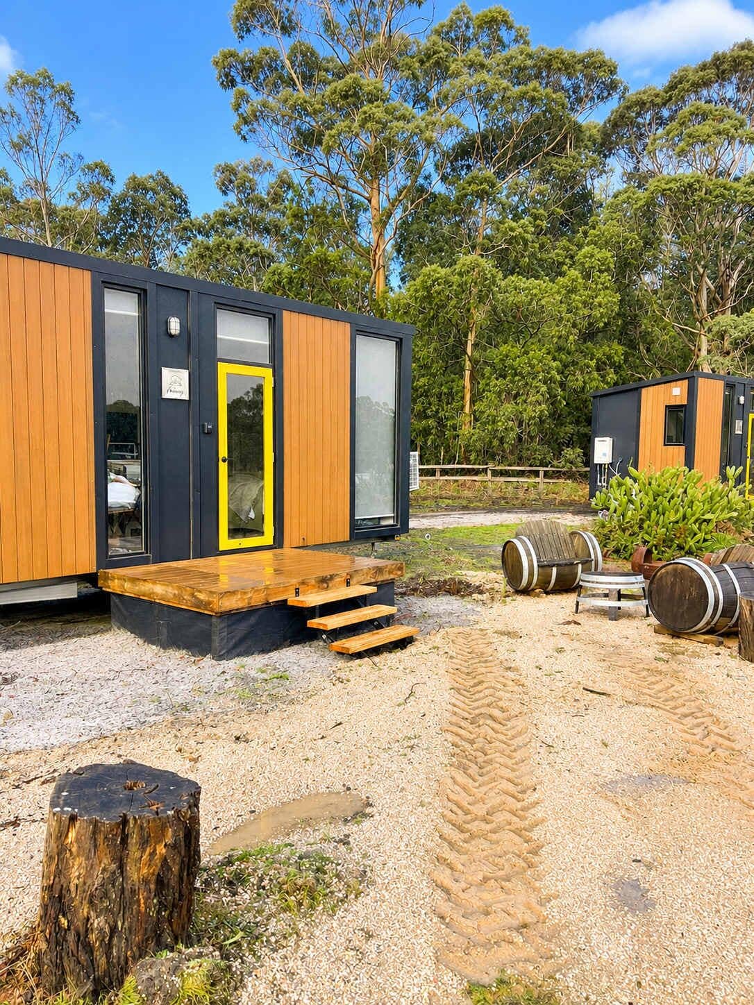 Une cabane moderne dotée d’une terrasse en bois, d’une porte et d’une fenêtre.