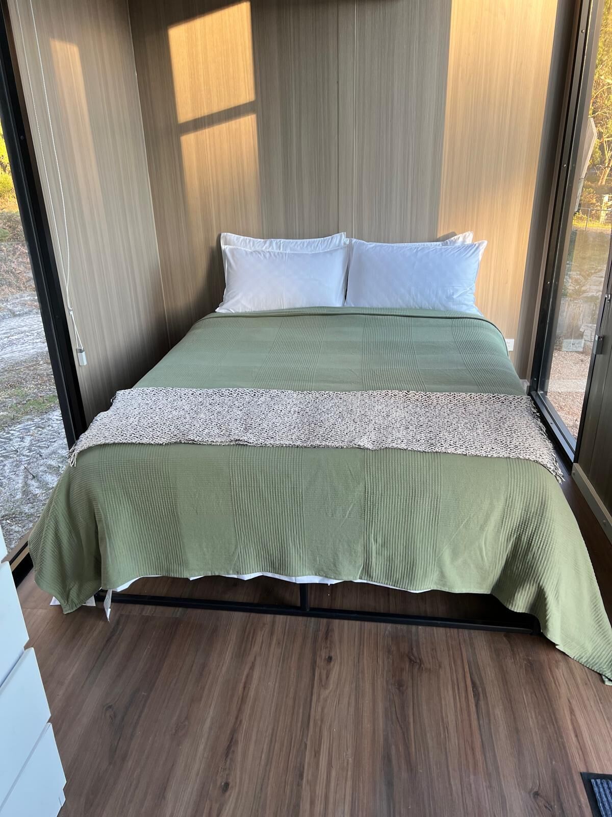 Un lit avec une couvre-lit verte et blanche, des oreillers blancs et une tête de lit en bois.