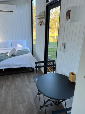 A bedroom with a bed, a small table, and a view of the outdoors.